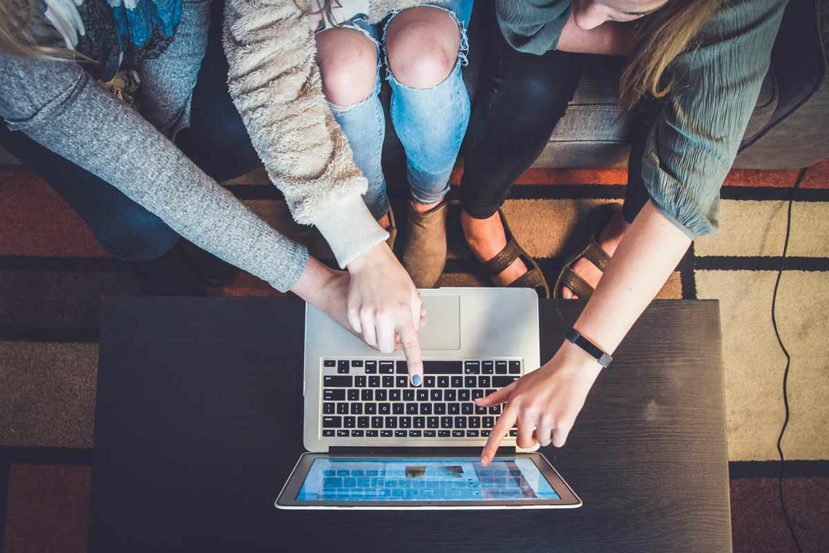 Three people collaborating and pointing at a laptop screen, symbolizing teamwork and learning in the field of digital marketing